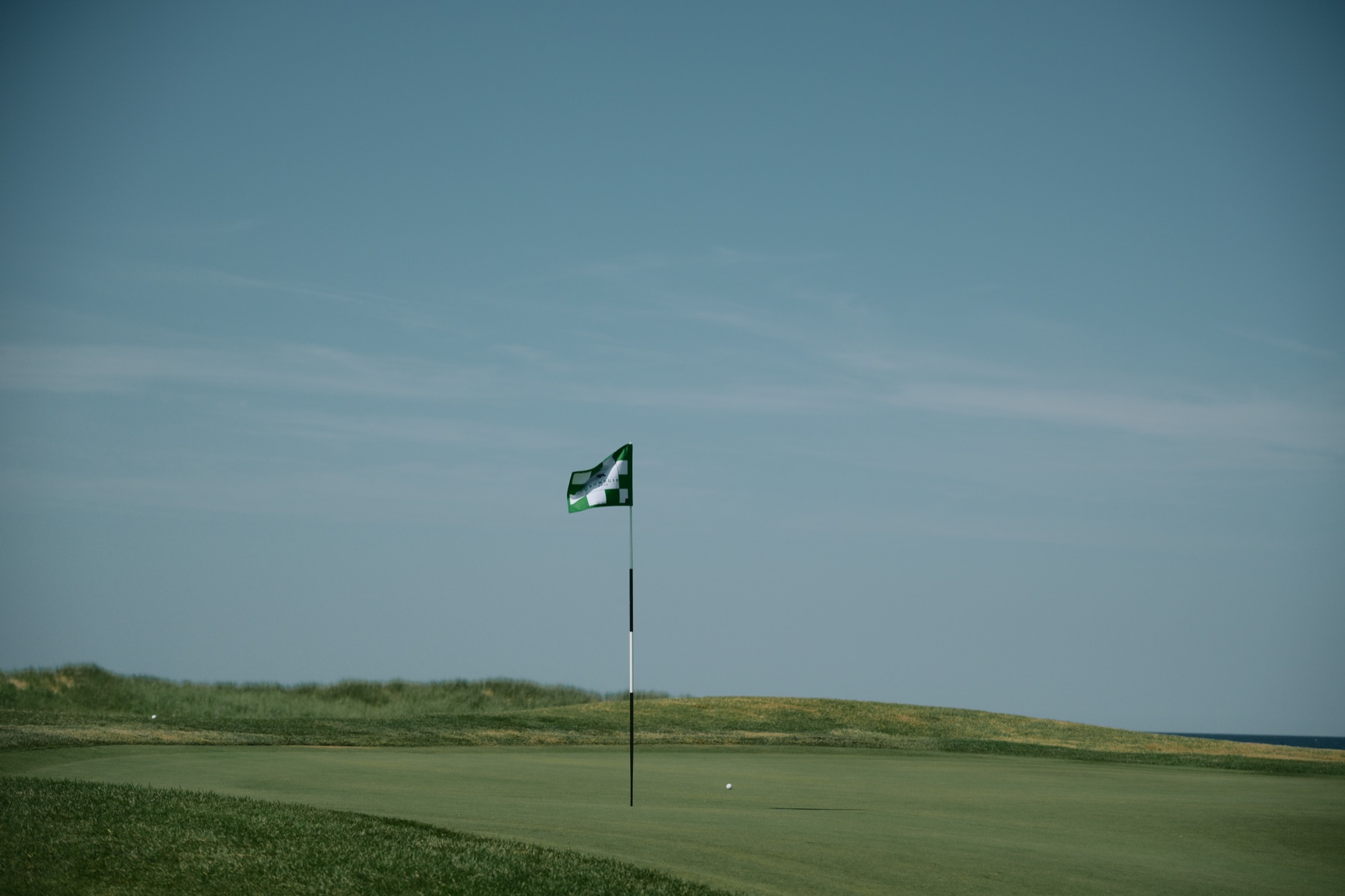 A green flag standing against the sky above a links green