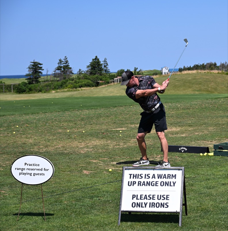 A player finishing a swing beside a warm-up range sign