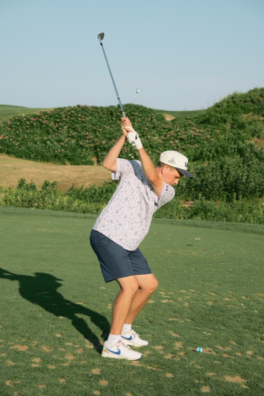 A player at the top of the backswing in front of a dune