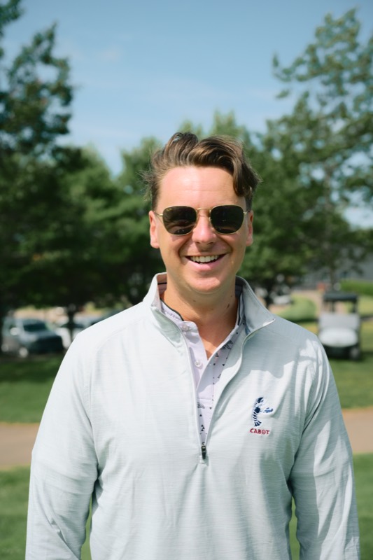 A player smiling in sunglasses and a quarter-zip