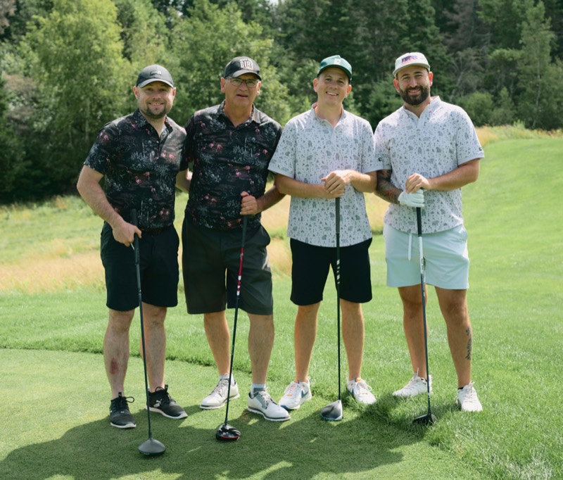 Four players posing with drivers on a tee