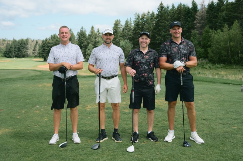 Four players standing behind their drivers on a tee box
