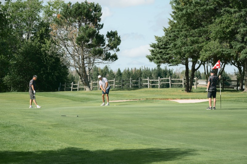Three players around a green with a Canadian flag pin